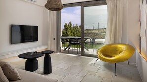 Una sala de estar moderna con un sofá, un televisor, una mesita y una silla amarilla. Posee un ventanal corredero que da a un espacio exterior con una mesa y sillas.