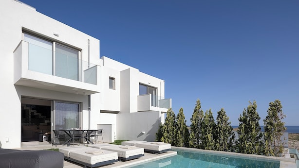 Una casa moderna con piscina, mobiliario exterior y vista al mar.