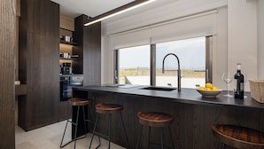 Una cocina moderna con armarios de madera oscura, una isla grande con taburetes, vistas por la ventana y una botella de vino sobre la isla.