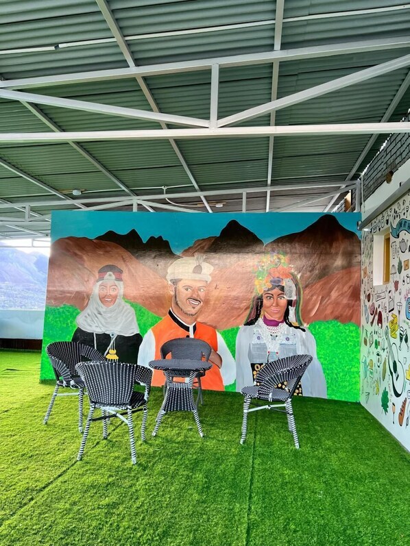 A mural with three figures seated on chairs under a metal roof structure.