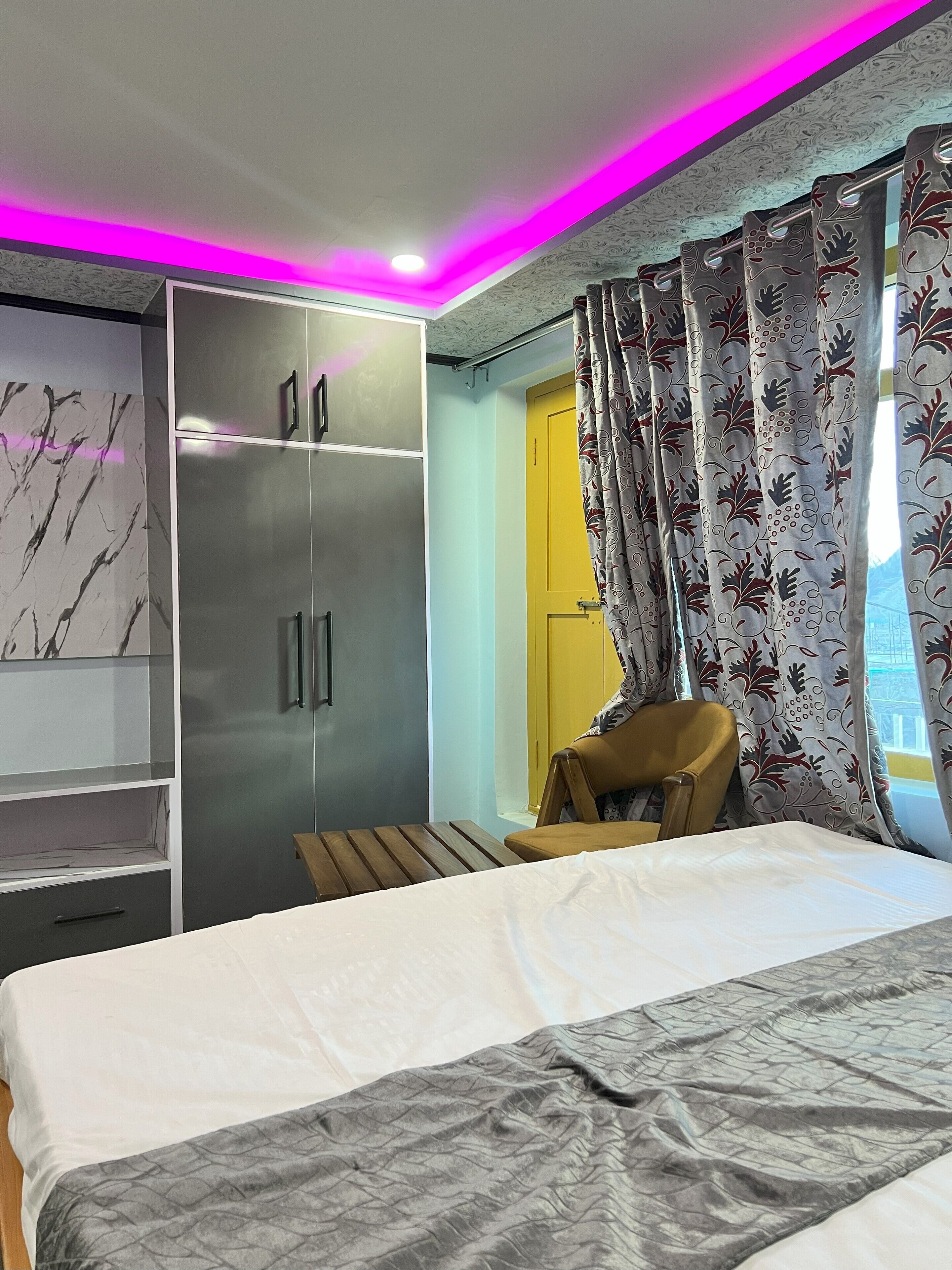 A bedroom with a bed, a wardrobe, a chair, and a window with curtains.