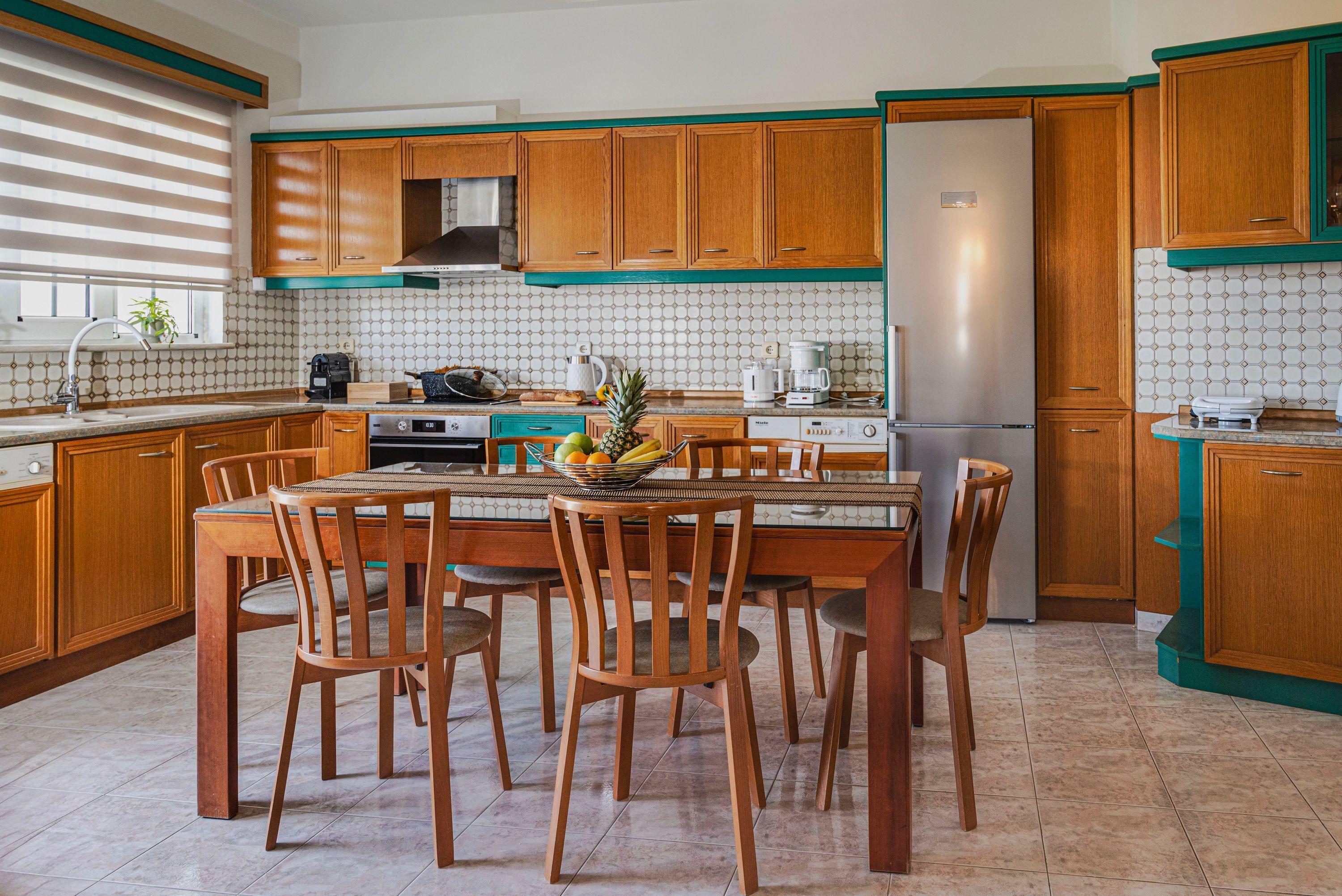A kitchen with wooden cabinets, a central island with chairs, a refrigerator, and various appliances.