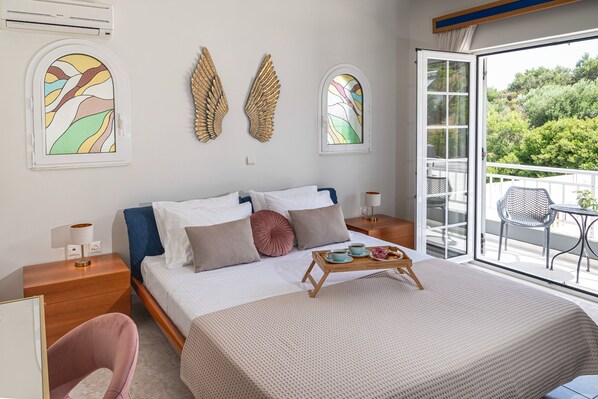 Una habitación de hotel con cama, una mesita de noche de madera, una silla pequeña y un balcón con una silla y una mesa.