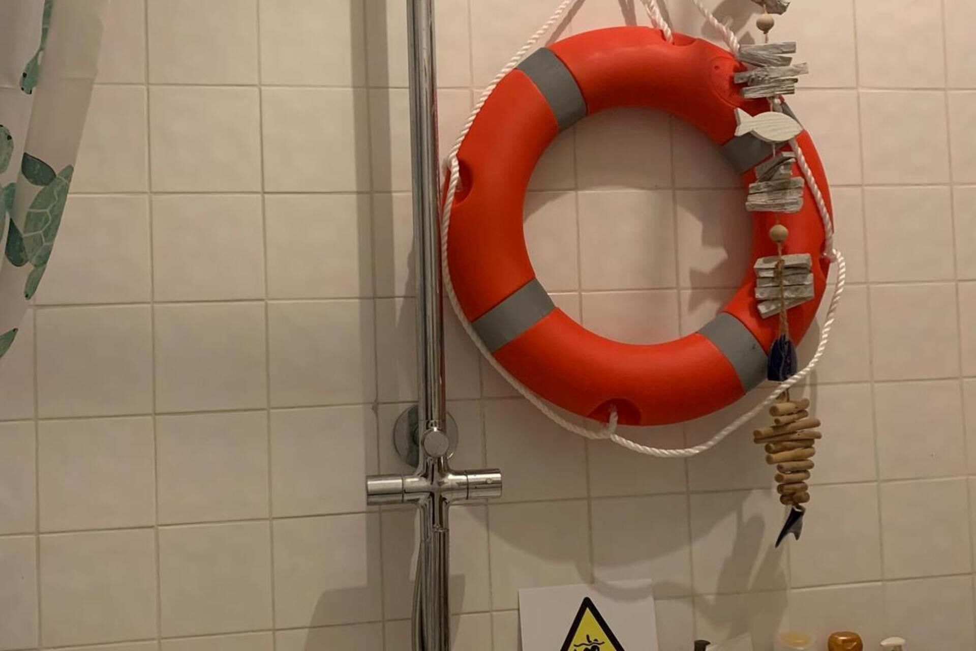A bathroom with a tiled wall, a shower, and a life preserver hanging on the wall.