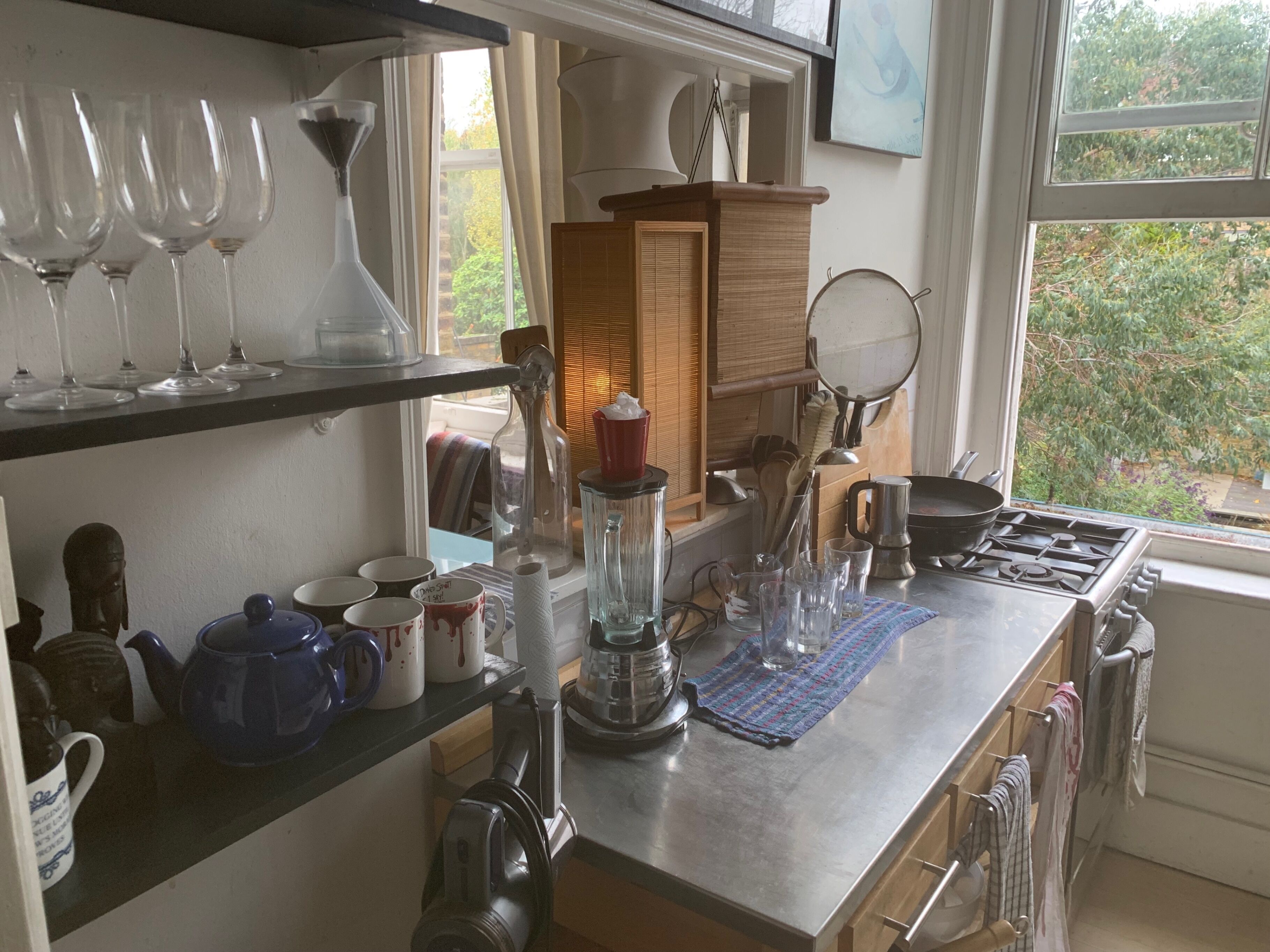 A kitchen with a stove, various kitchen utensils, and a window with a view of greenery.