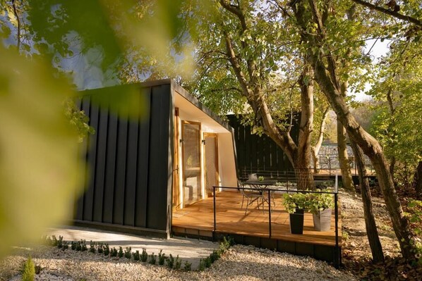 A modern outdoor structure with a wooden deck, surrounded by trees and gravel. - Blisku do Gradot Riverfront Cabins (Varvara)