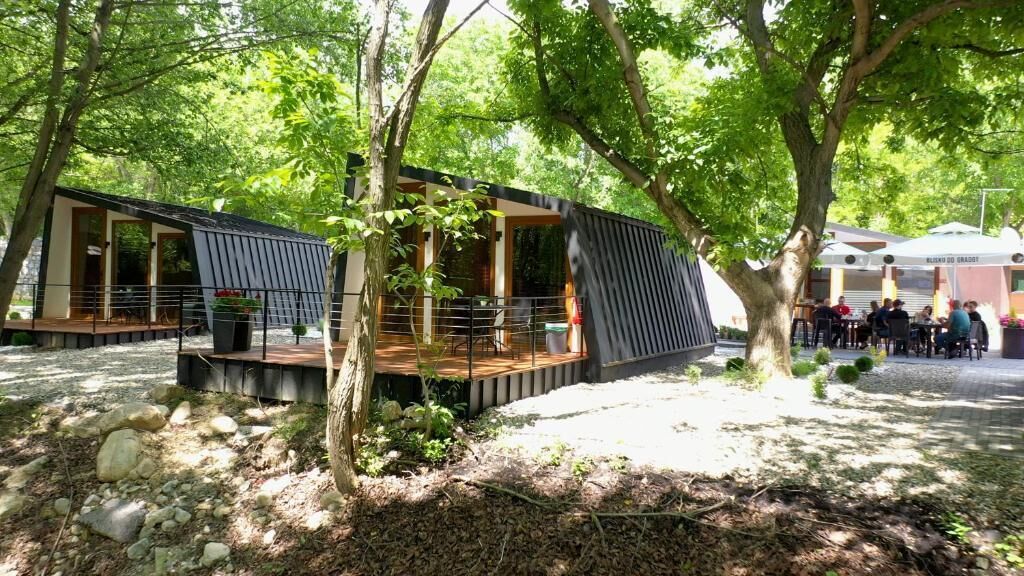 Un espace de restauration extérieur moderne, doté d’une terrasse en bois et de sièges, le tout entouré d’arbres.