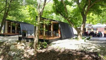 Un espace de restauration extérieur moderne, doté d’une terrasse en bois et de sièges, le tout entouré d’arbres.