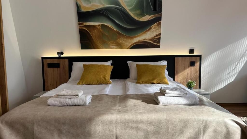 Una cama doble con una colcha color beige, dos almohadas y toallas dobladas.