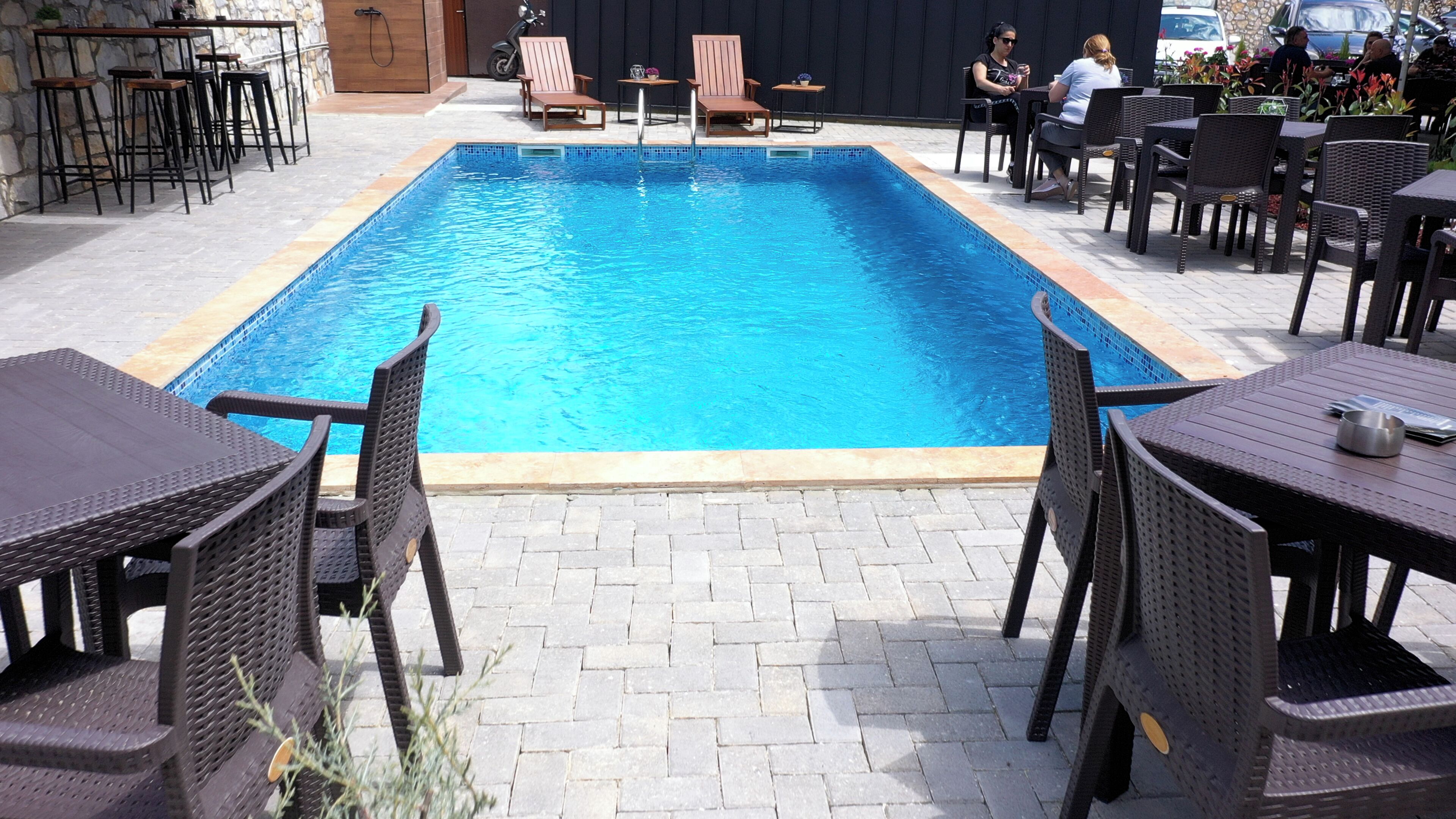 Et rektangulært swimmingpool med flisekant, omgivet af udendørs siddepladser med fletborde og stole.