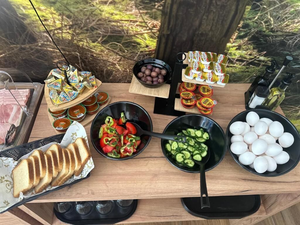 A wooden table with various food items including sliced bread, a salad, cucumbers, eggs, and condiments.