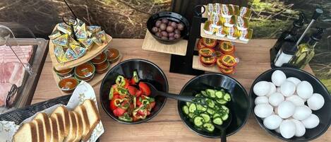 A wooden table with various food items including sliced bread, a salad, cucumbers, eggs, and condiments.