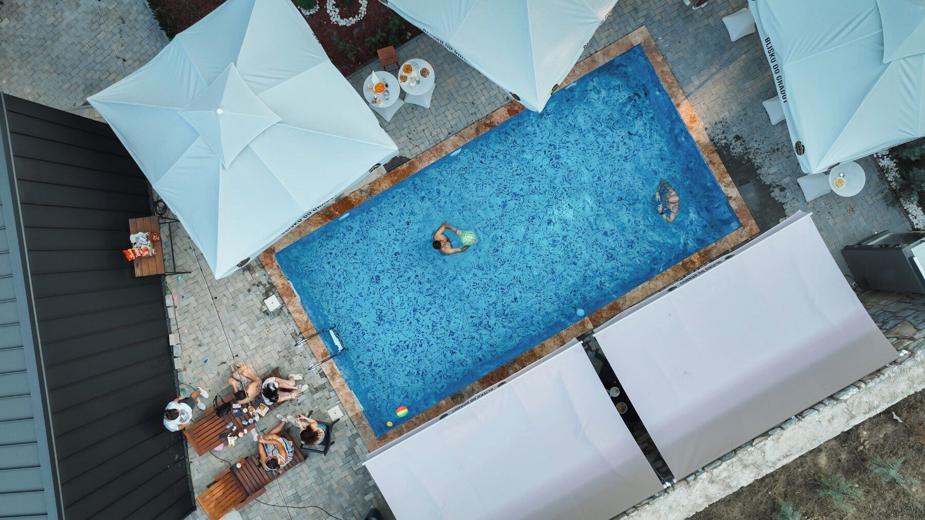 Una piscina al aire libre con sillas de descanso y sombrillas, rodeada de una zona pavimentada.