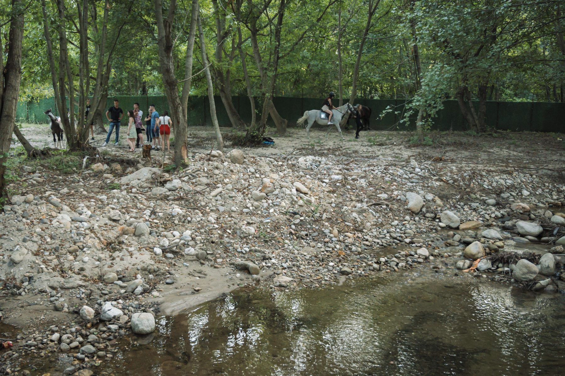 Un ruisseau aux rives rocheuses, avec des personnes qui s'y promènent et un cheval à proximité.