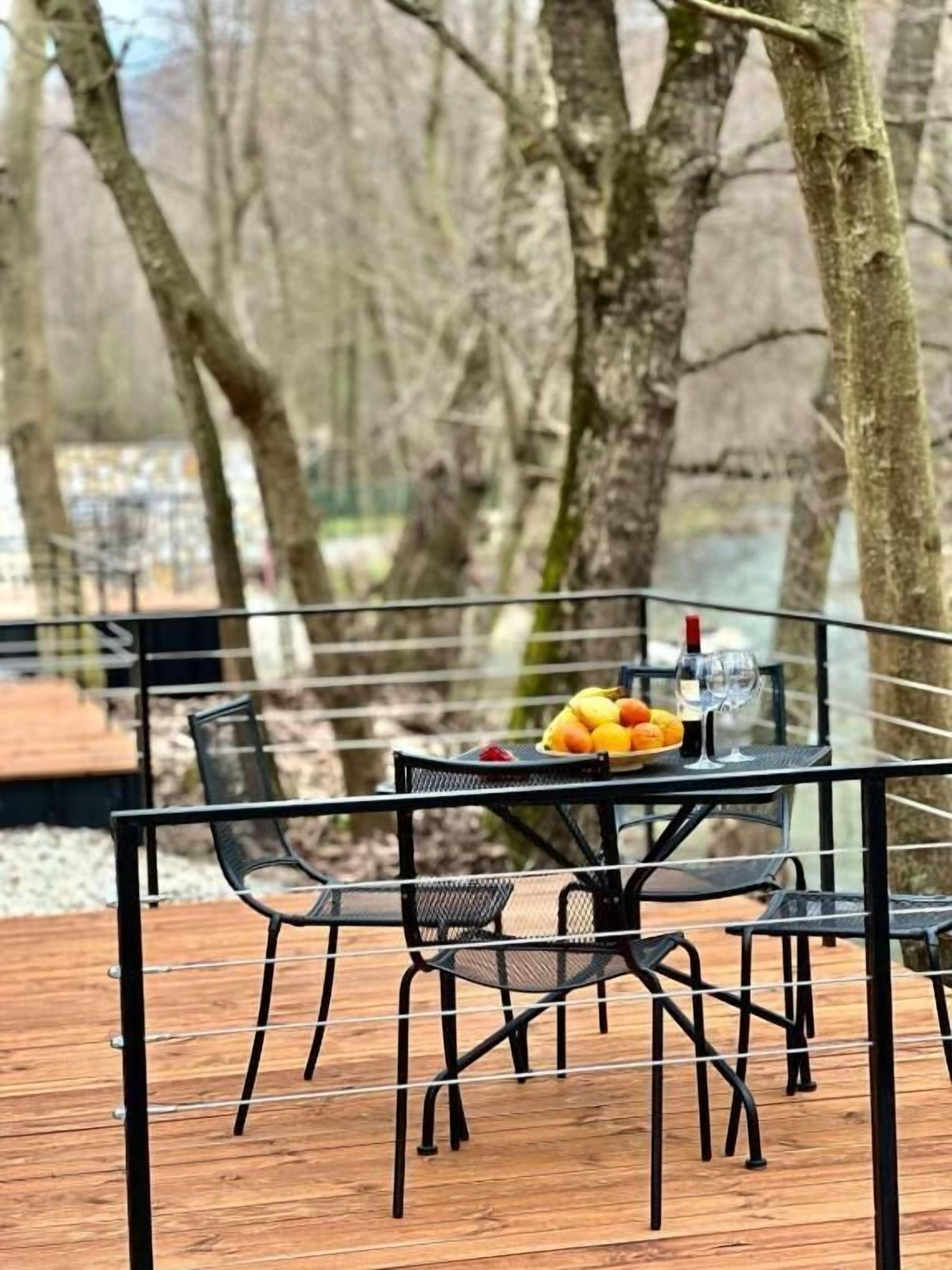 Un'area pranzo all'aperto con tavolo e sedie, una ciotola di frutta e un bicchiere di vino.