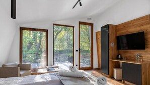 A modern bedroom with a bed, two windows with blinds, a TV, and a wooden cabinet. - Blisku do Gradot Riverfront Cabins (Varvara)