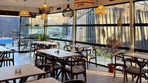 A restaurant with wooden tables and chairs, large windows, and hanging pendant lights. - Blisku do Gradot Riverfront Cabins (Varvara)