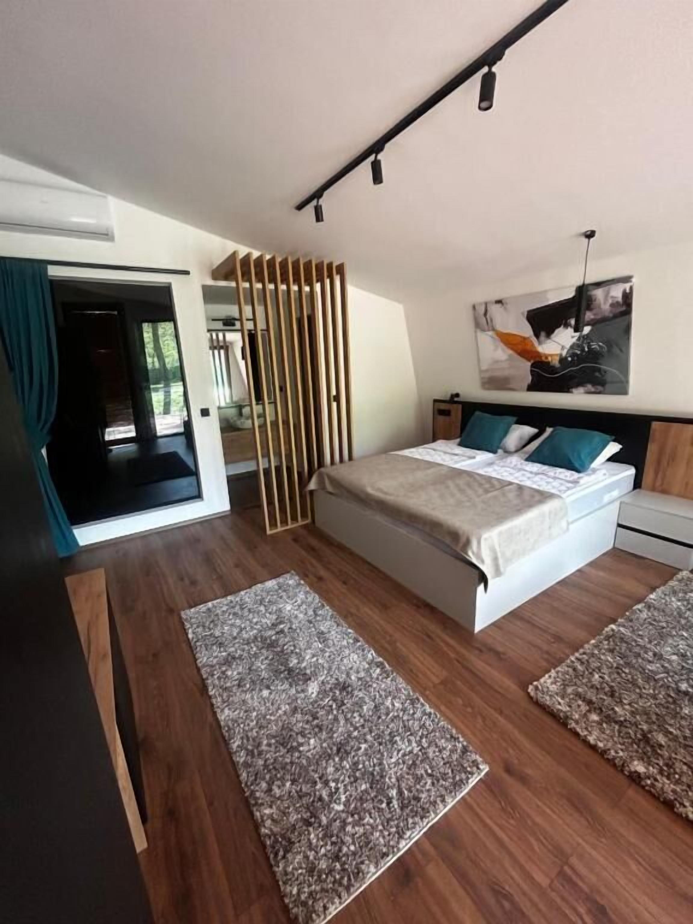 A modern bedroom with a bed, two rugs, a wooden partition, and a painting on the wall.