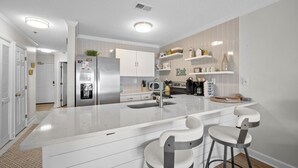 A modern kitchen with white cabinetry, a central island with bar stools, and built-in appliances. - Sunny Side Up at Villa Capriani Resort | Unit 108A | North Topsail Beach, NC (North Topsail Beach)