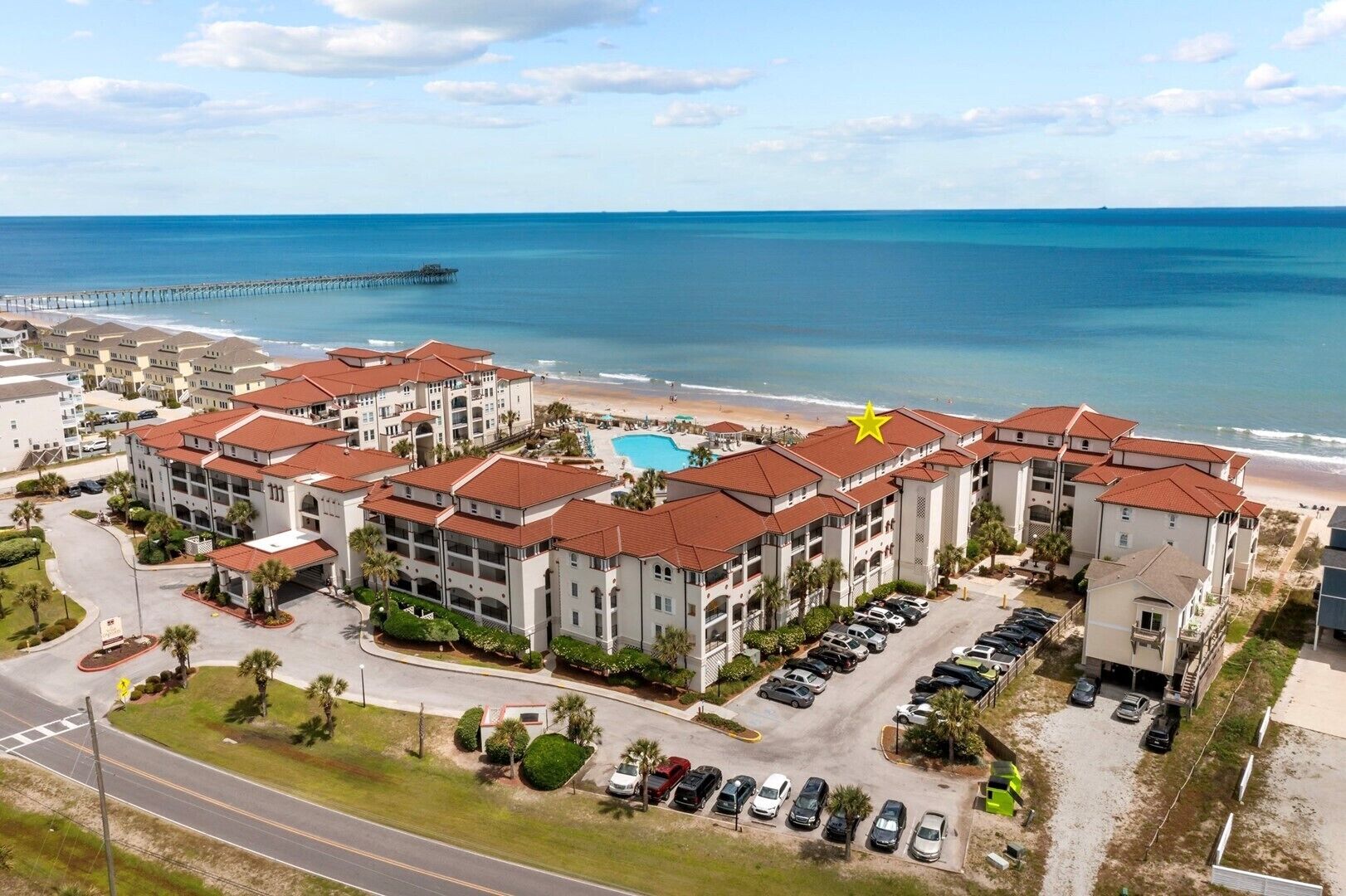 A beachfront hotel with multiple buildings, a swimming pool, and a pier in the background.