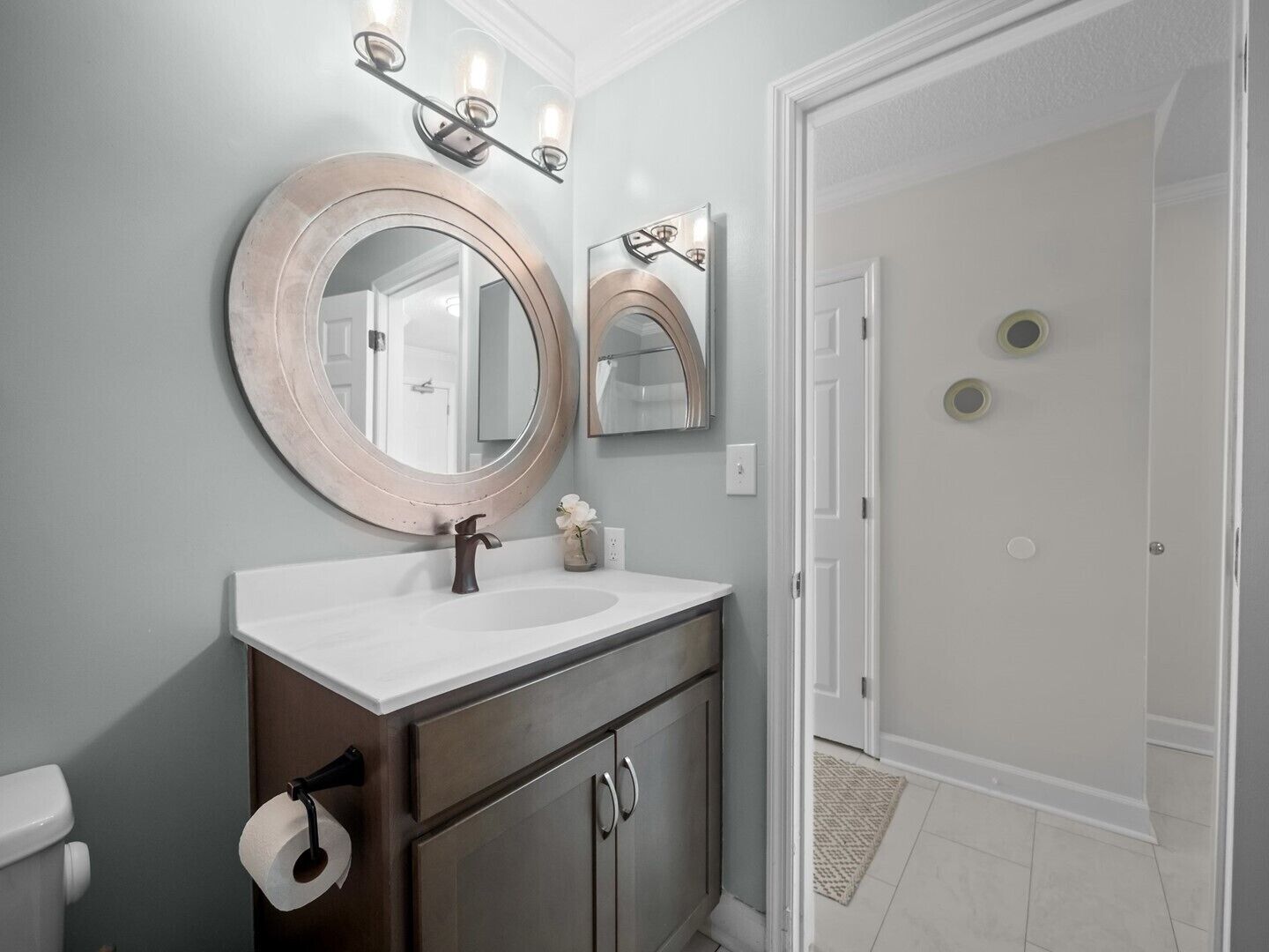 A bathroom with a round mirror, a white sink, and a toilet. There are two wall-mounted lights above the mirror.