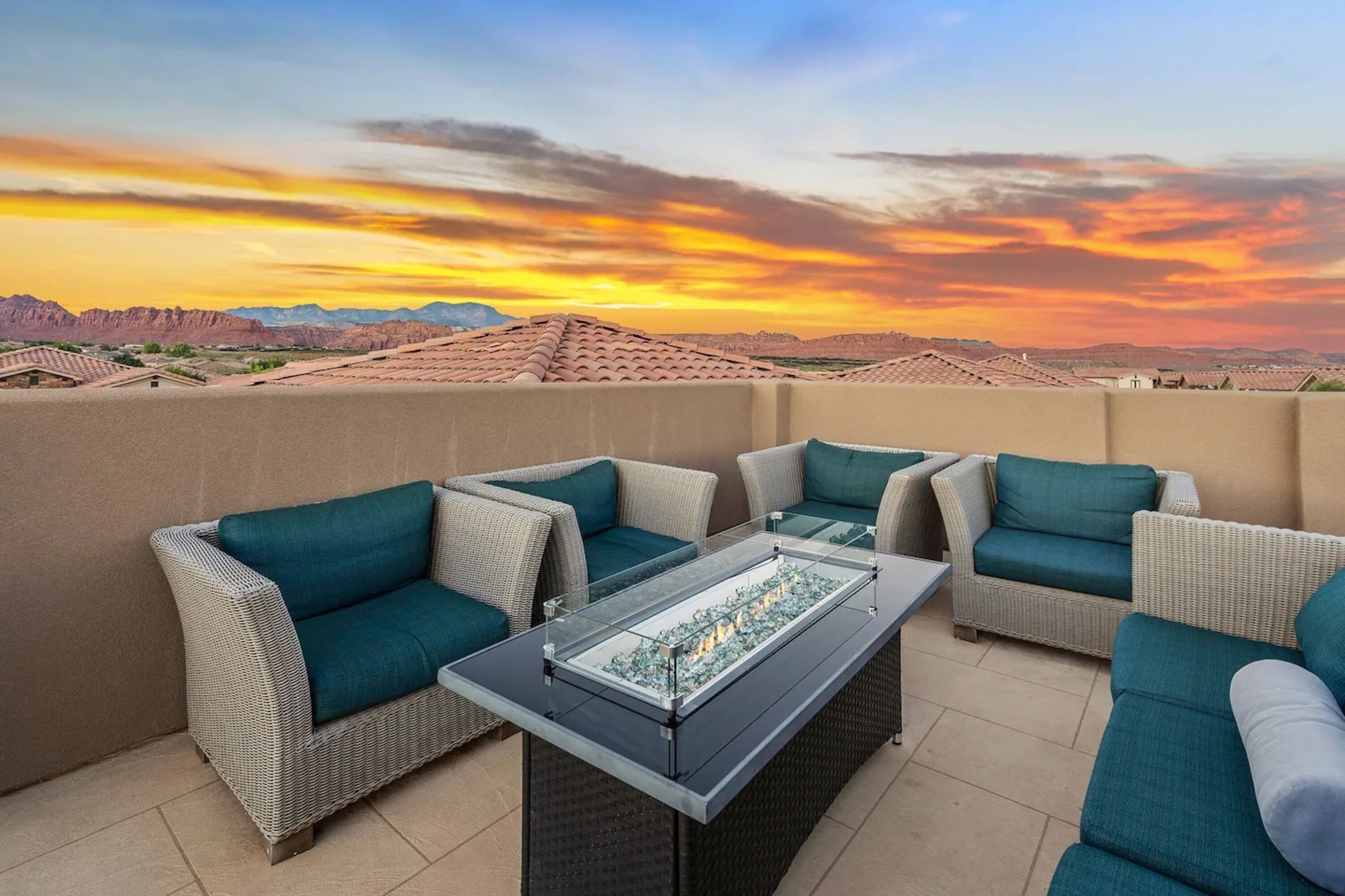 Eine Dachterrasse mit Korbmöbeln und einem Tisch mit Glasplatte, mit Blick auf eine Wüstenlandschaft bei Sonnenuntergang.