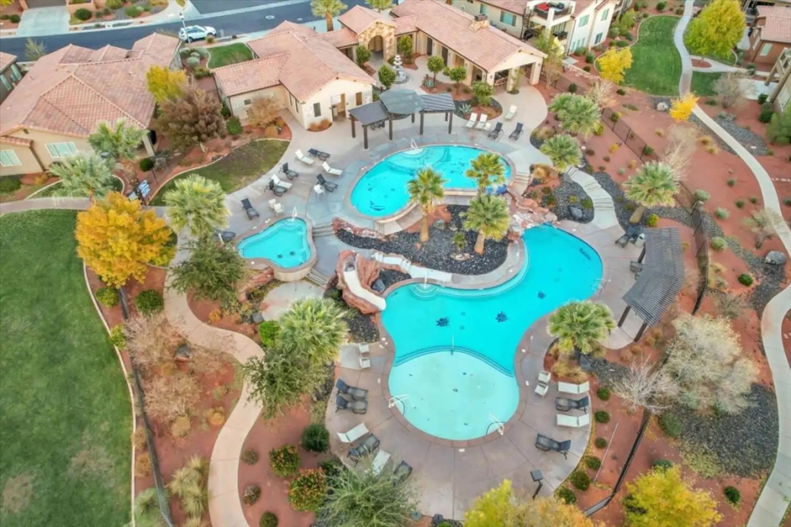 Un quartier résidentiel doté d’une grande piscine, entourée de chaises longues et de palmiers.