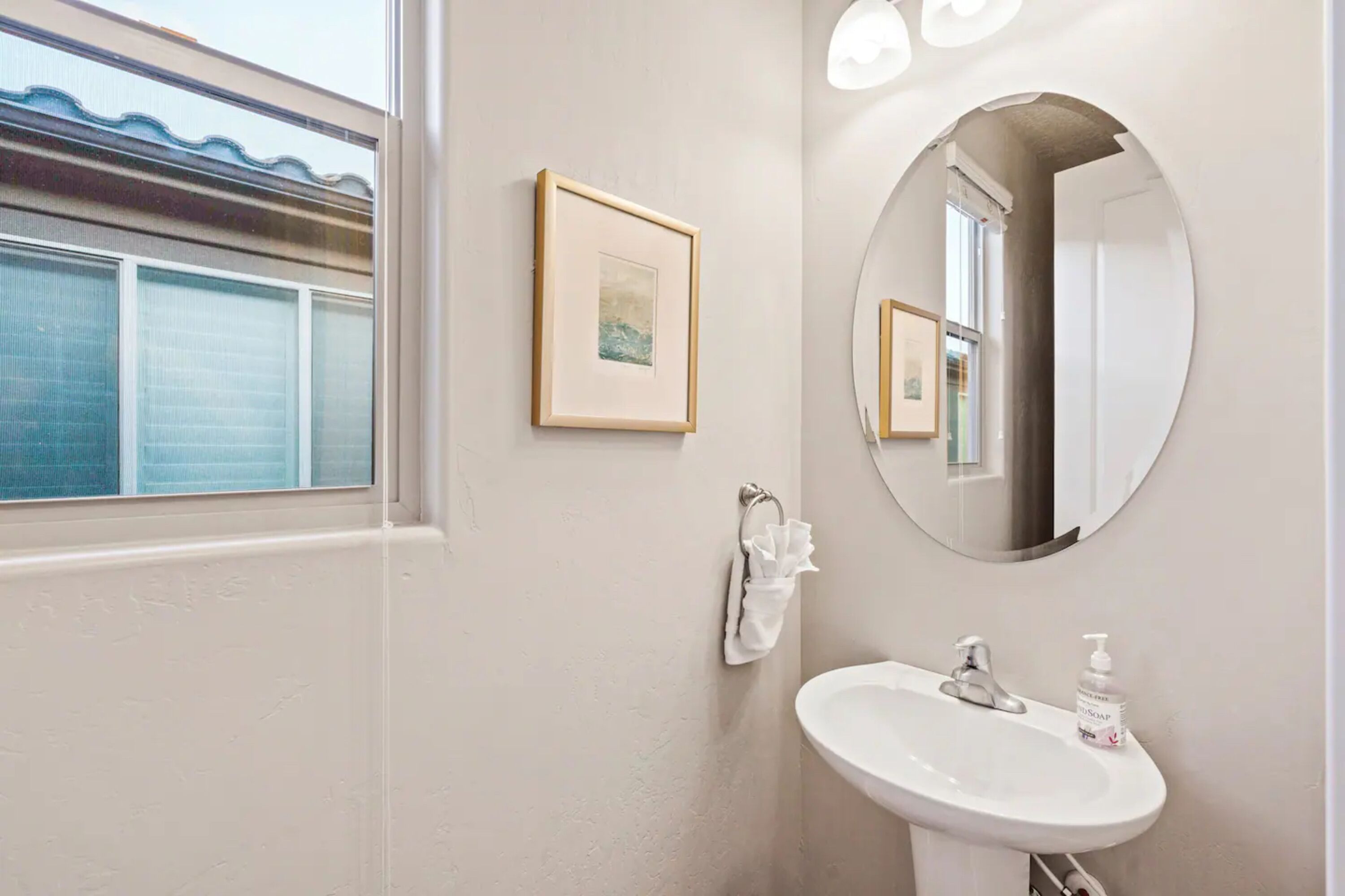 Een badkamer met een witte wastafel, een ingelijst schilderij aan de muur, een handdoek aan een rek en een grote spiegel.