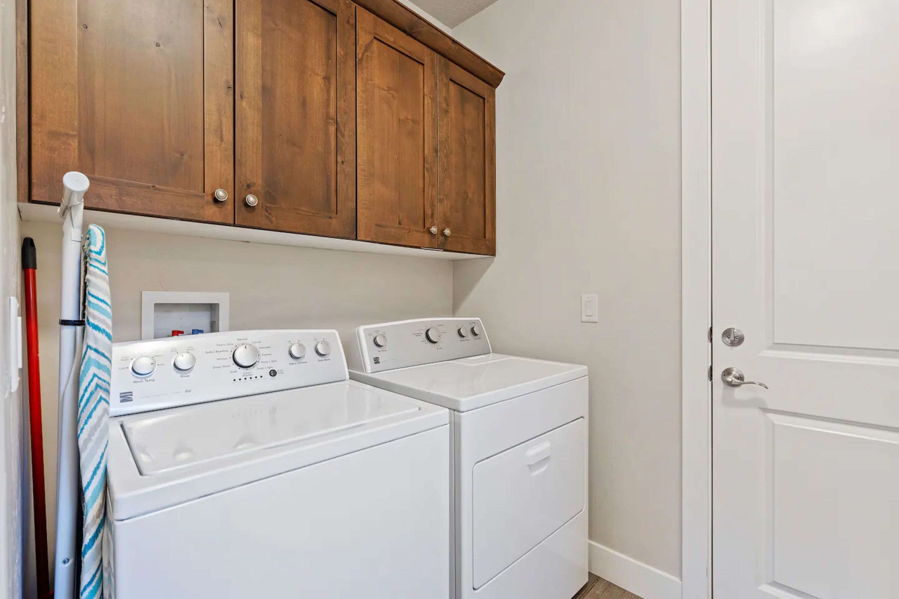 A laundry area with two white front-loading washers and dryers, wooden cabinets above, and a white door to the right.