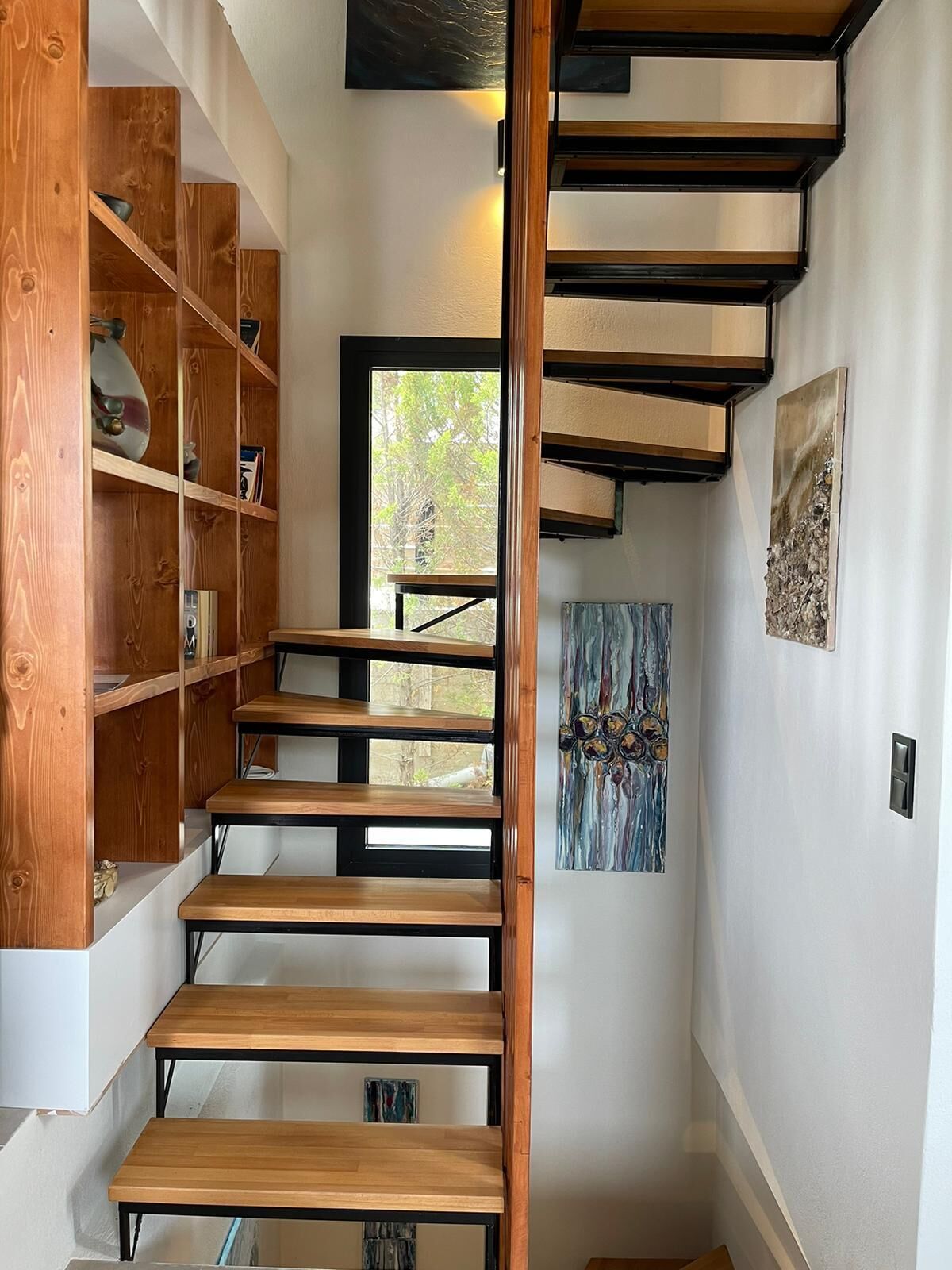 A modern staircase with wooden steps and black railings, leading to a room with white walls and a window.
