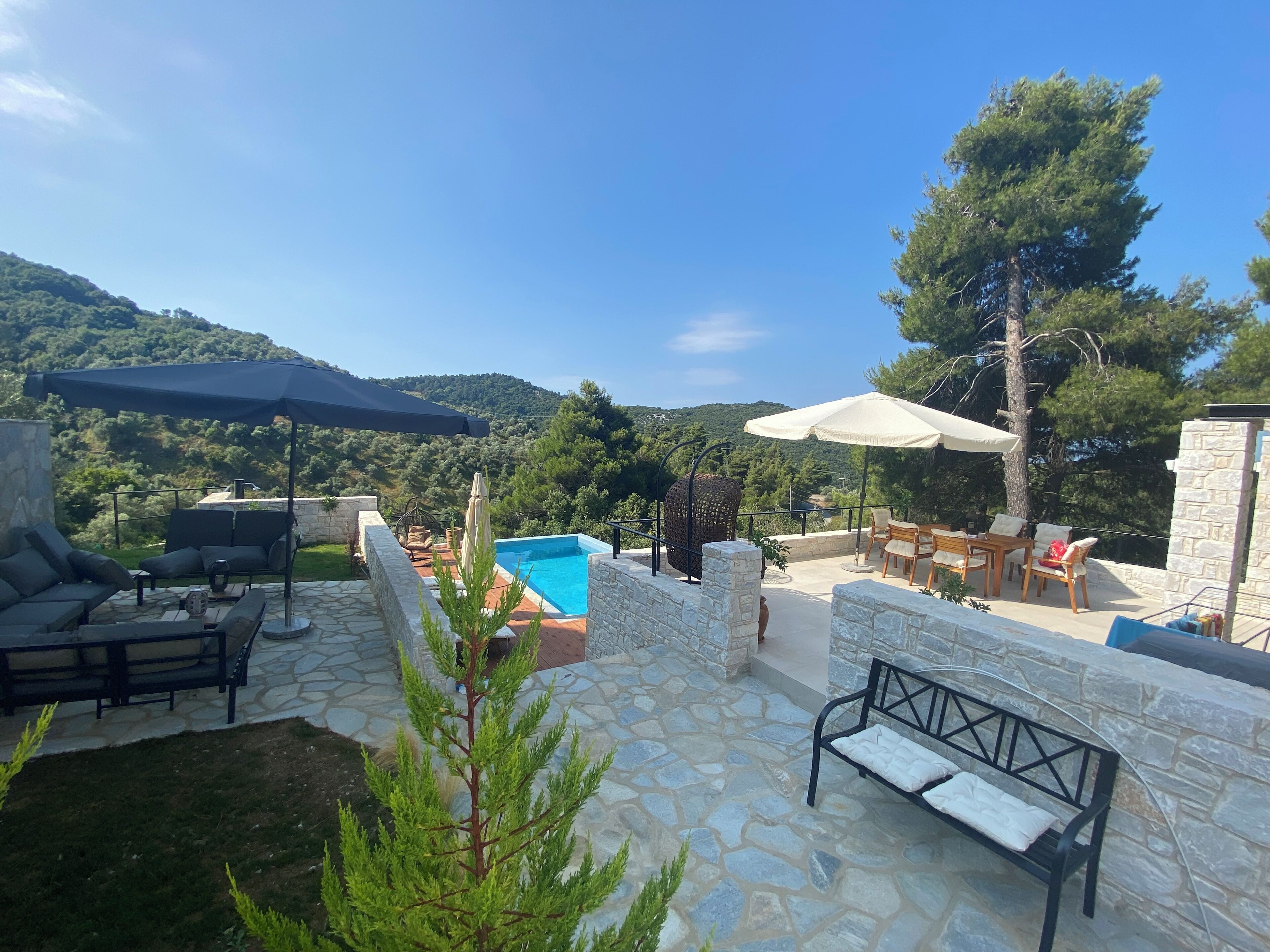 Eine Steinterrasse mit Gartenmöbeln, einem Swimmingpool und Blick auf eine gebirgige Landschaft.