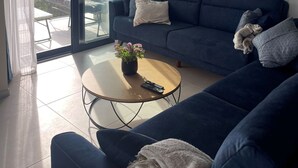 Un salon moderne avec un canapé bleu foncé, une table basse ornée d’une plante en pot et un grand tableau abstrait accroché au mur.