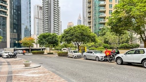 Une rue moderne en milieu urbain, avec des voitures garées, des scooters de livraison et un livreur.