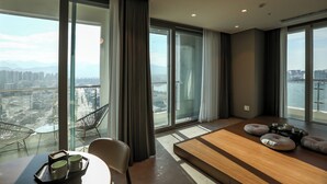 A modern hotel room with large windows, a wooden table with a tray of mugs, and a seating area with cushions. - Hotelaround Sokcho (Sokcho)