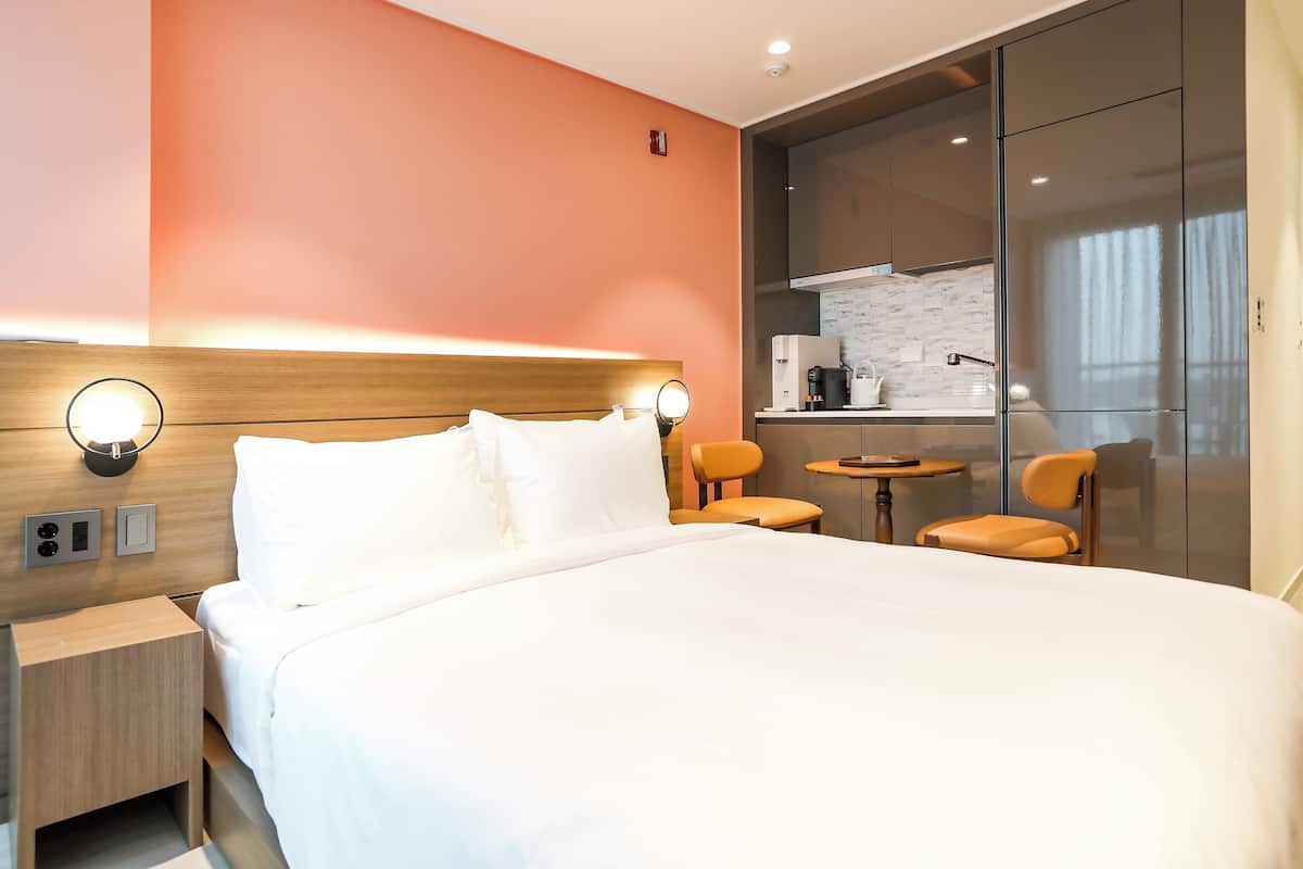 Een hotelkamer met een groot bed, nachtkastjes, een eettafeltje, twee stoelen en een kitchenette op de achtergrond.