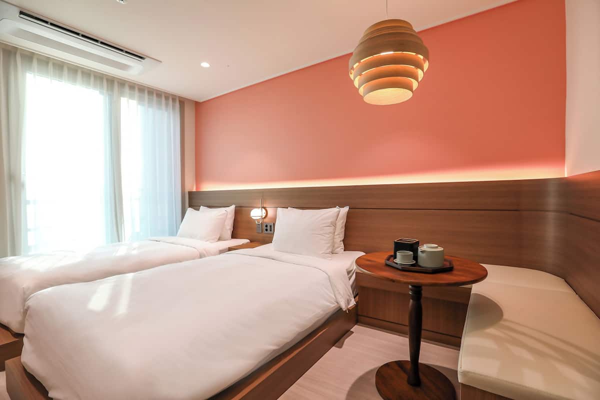 Een hotelkamer met twee bedden, een houten hoofdbord, een nachtkastje met een lamp en uitzicht op het omliggende landschap.