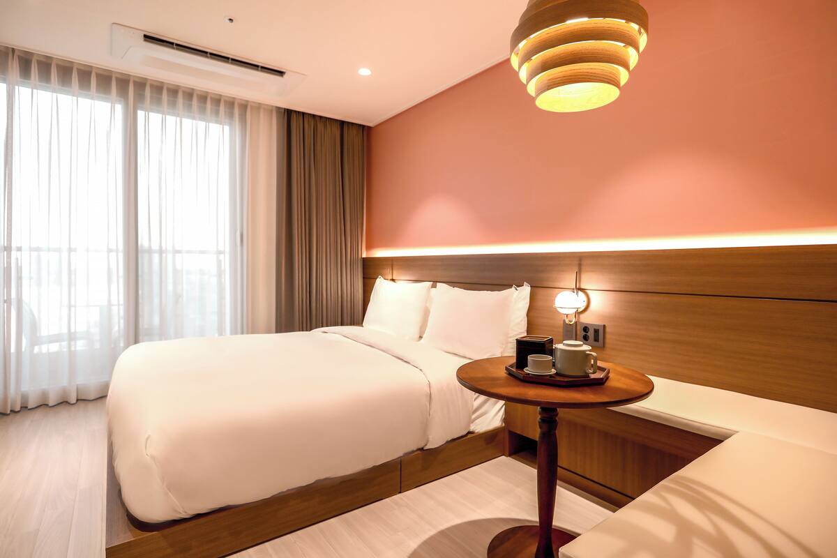 Een hotelkamer met een groot bed, een nachtkastje met kop en schotel, en een moderne hanglamp.