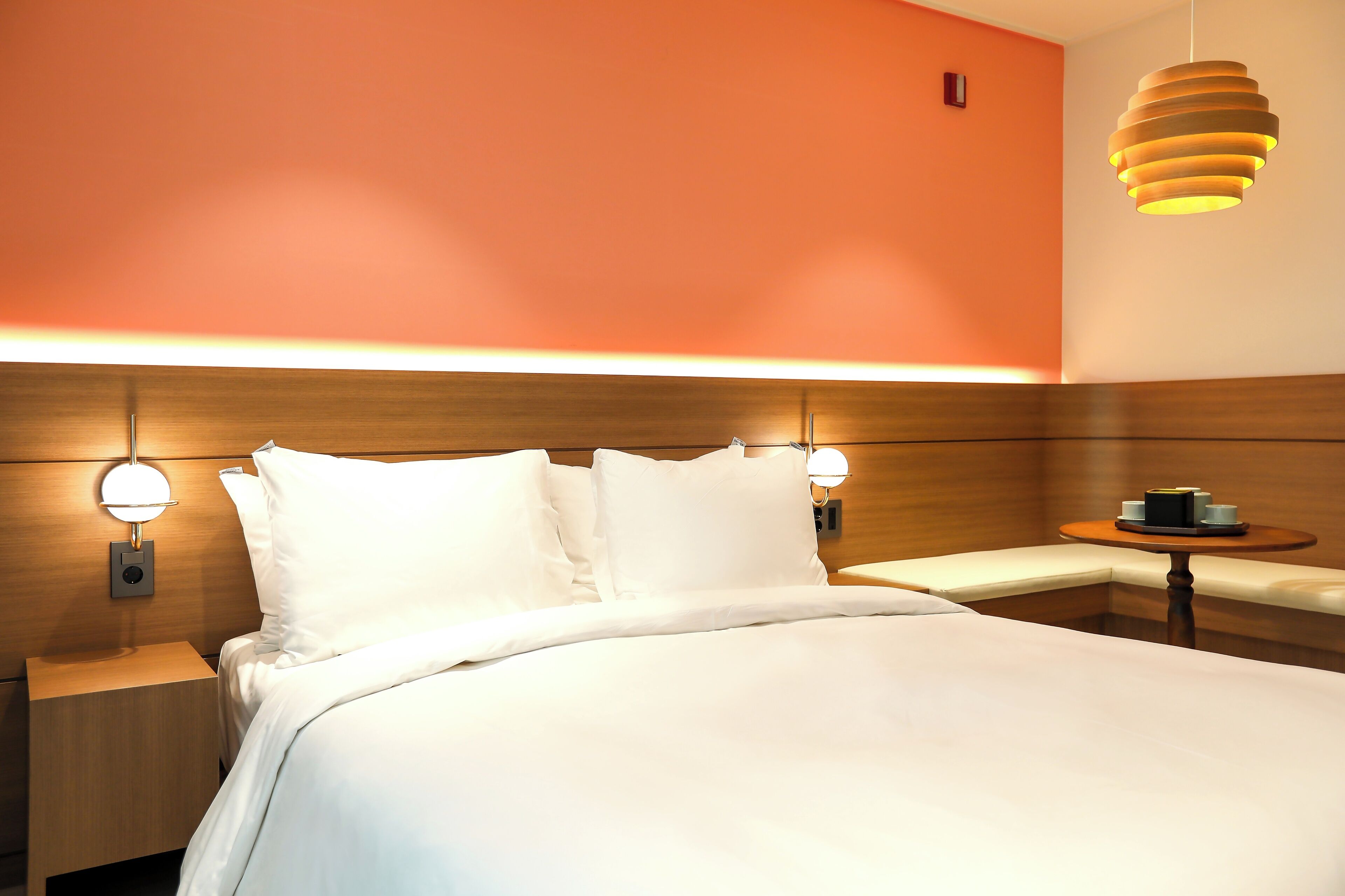 Habitació d'hotel amb un llit gran, dues taules de nit amb làmpades, una taula rodona petita amb una làmpada i un llum fixat a la paret.
