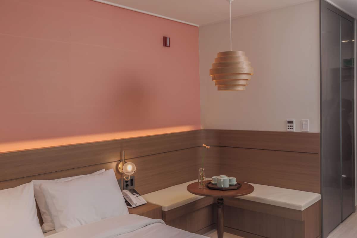 Een moderne hotelkamer met een houten hoofdeinde, een nachtkastje met een lamp, een klein tafeltje met een dienblad en een paneel bevestigd aan de muur.