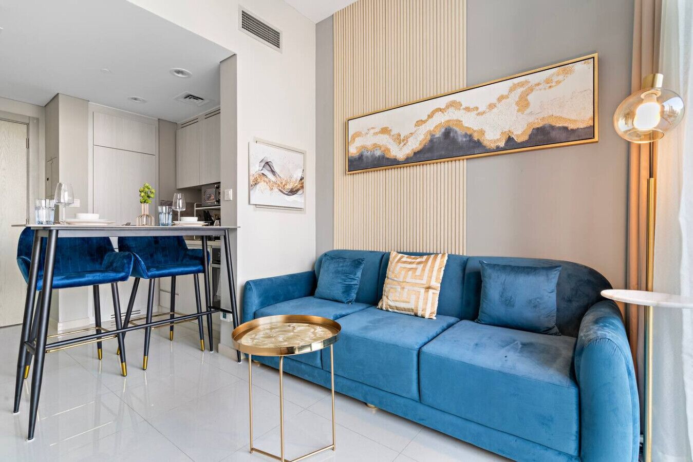 Una sala moderna con un sofá azul, un comedor con barra y una cocina al fondo.