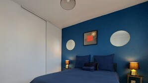 Un dormitorio moderno con una cama grande, dos mesitas de noche con lámparas, un espejo circular y una obra de arte en la pared.