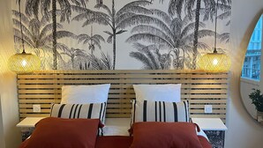 A bedroom with a bed, two bedside tables, a wall mural of palm trees, and two hanging lamps. - Cosy T2, Notre-Dame church view, downtown, new (Le Havre)