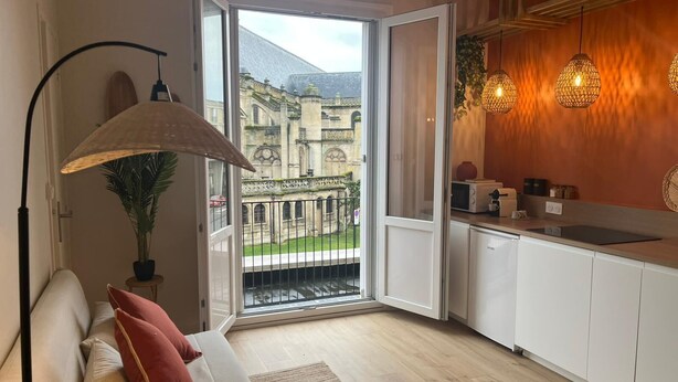 A modern kitchen with a view of a historic building, a dining area with a sofa, and a large window. - Cosy T2, Notre-Dame church view, downtown, new (Le Havre)