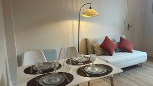 A dining area with a table set for four, a sofa with cushions, and a lamp. - Cosy T2, Notre-Dame church view, downtown, new (Le Havre)