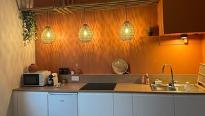 A modern kitchen with a wooden backsplash, pendant lights, a microwave, a toaster, and a sink. - Cosy T2, Notre-Dame church view, downtown, new (Le Havre)