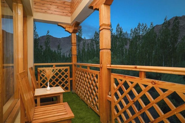A wooden balcony with a table and chairs, a lattice railing, and a view of a forested mountain range. - The Countryside Villa Ladakh (Leh)