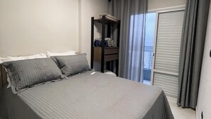 Ein Schlafzimmer mit einem großen Bett, einem Kleiderschrank, einem kleinen Tisch und einem Fenster mit Vorhängen.