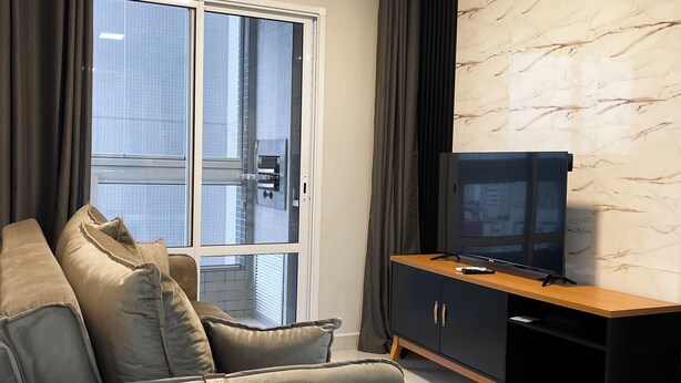 Ein modernes Wohnzimmer mit einem grauen Sofa, einer schwarzen Unterhaltungsecke und einem Fernseher.