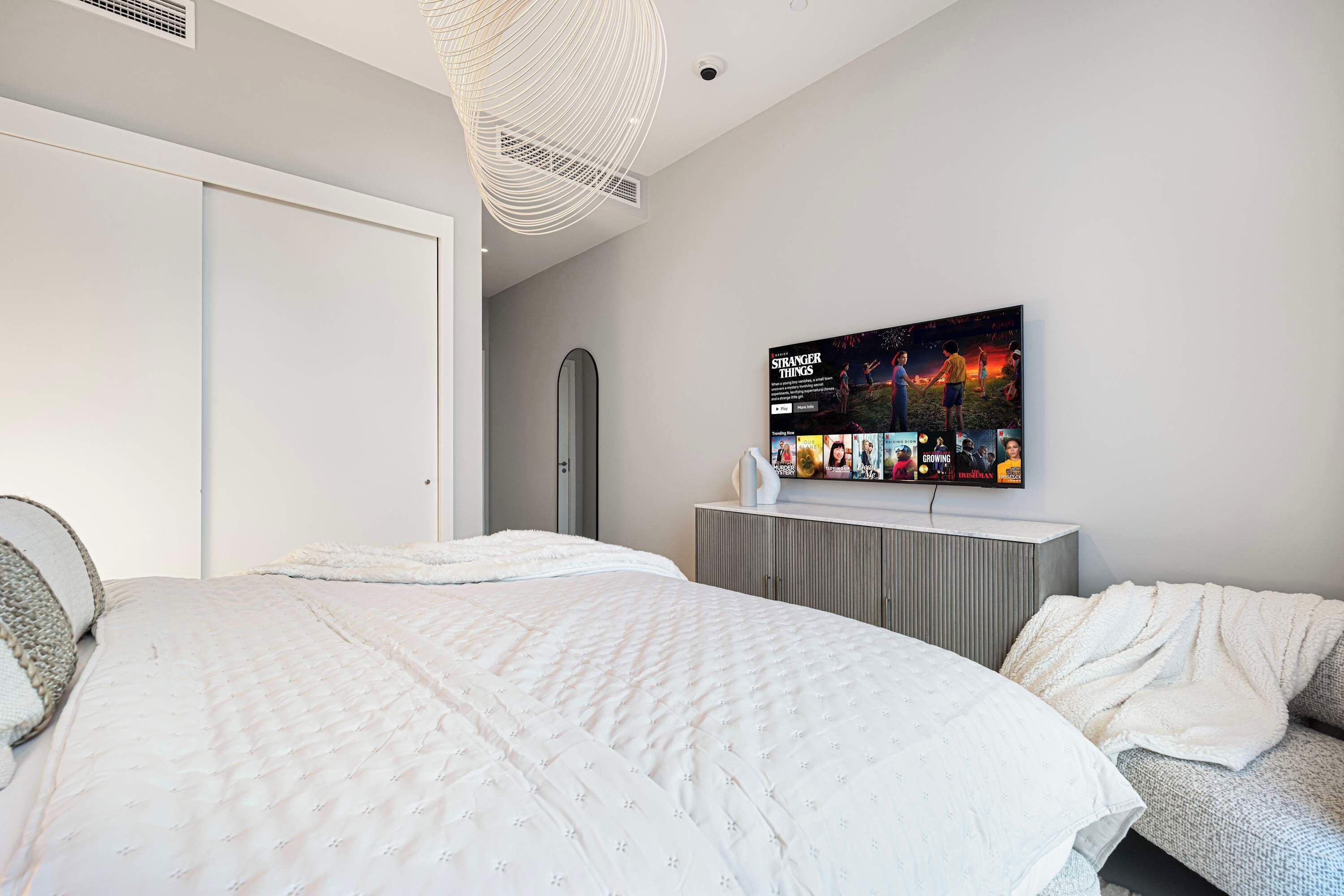 A modern bedroom with a large bed, a television mounted on the wall, and a wardrobe.