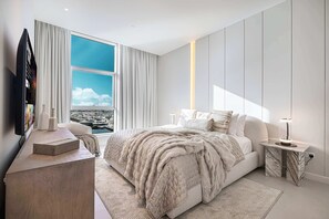 Ein modernes Schlafzimmer mit einem großen Bett, einem Fernseher, einem Schreibtisch und Blick auf den Hafen.